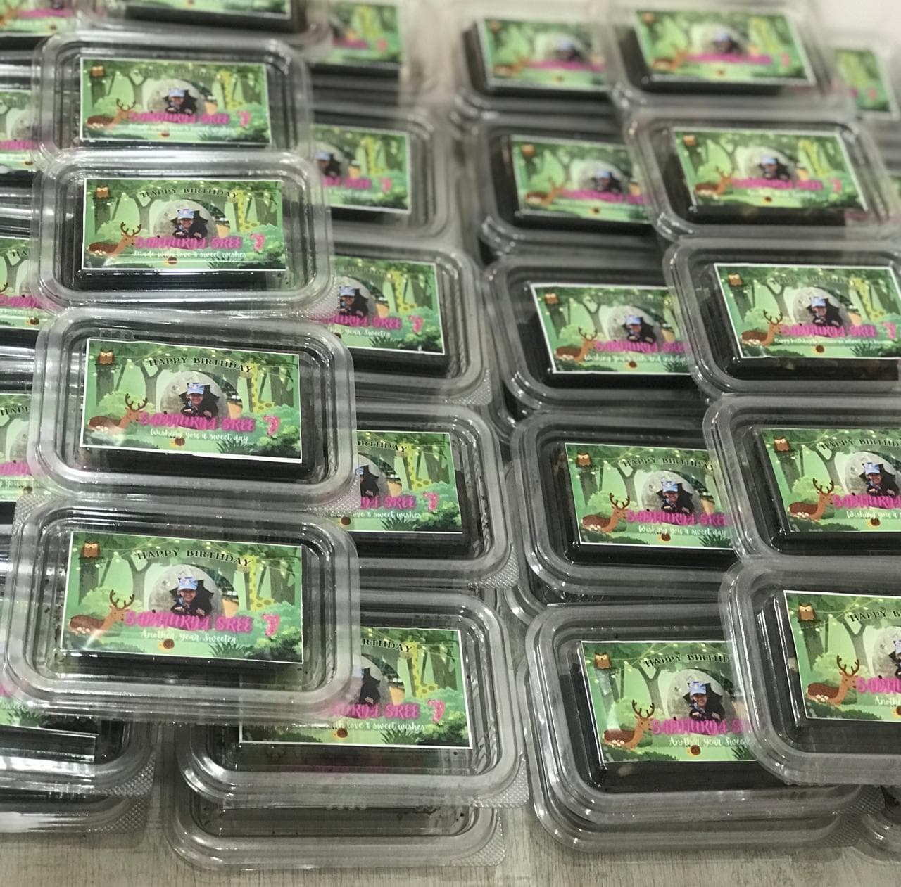 Stacked clear plastic containers of brownies with personalized forest-themed birthday labels and photos.