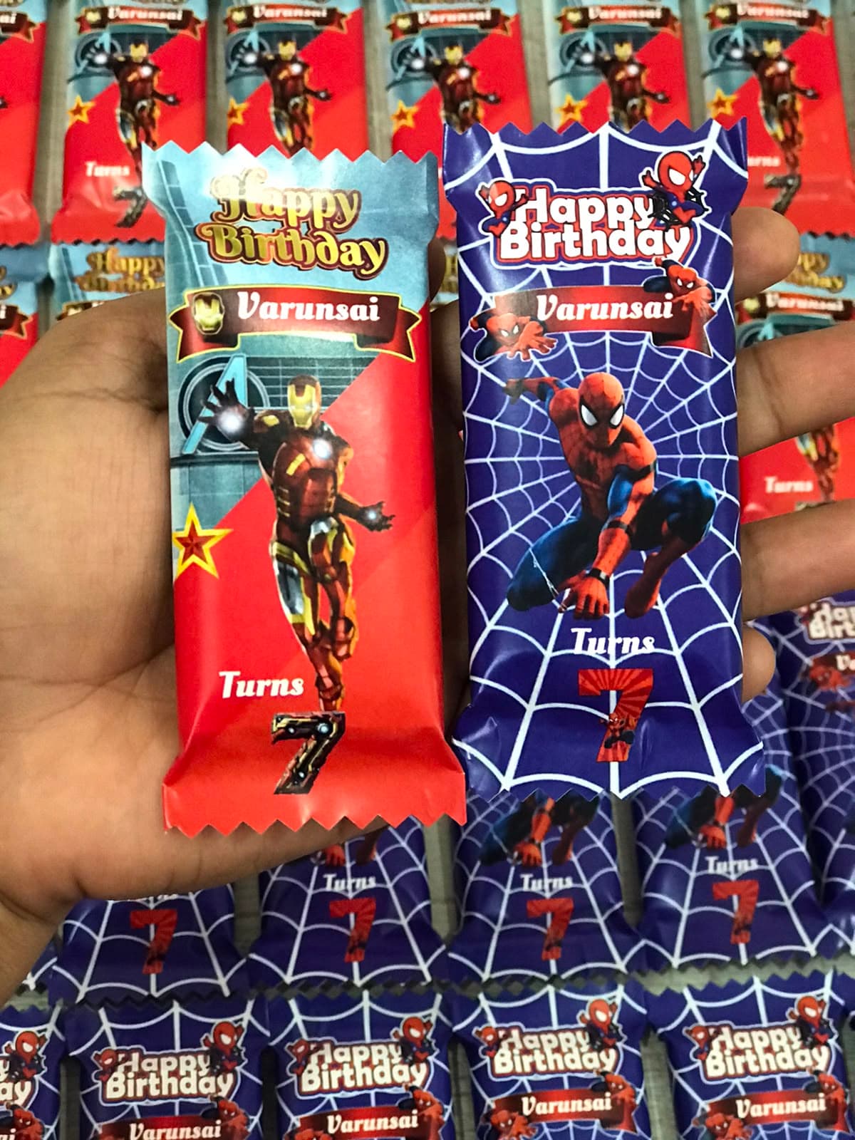 Hand holding Iron Man and Spider-Man birthday treats labeled Varunsai turns seven.