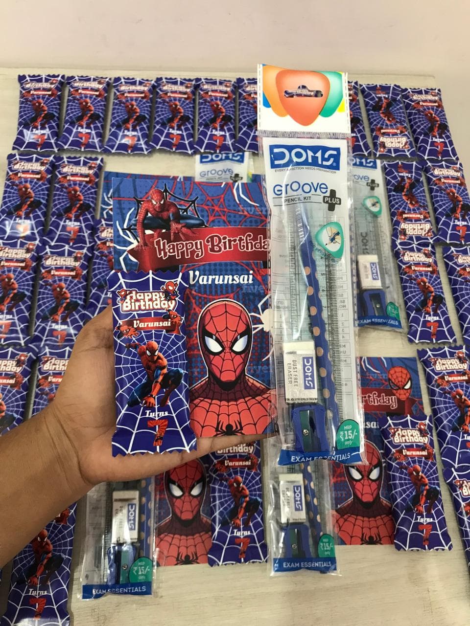 Hand holding a Spider-Man birthday gift set with stationery and personalized treats for Varunsai.